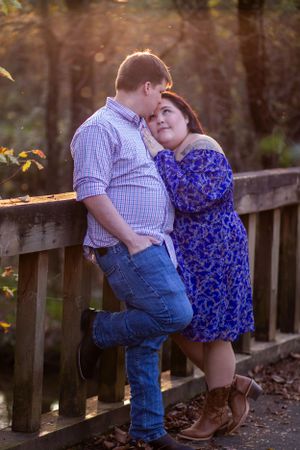 A couple shares an intimate moment against a wooden railing at sunset.