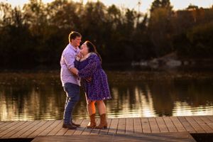 A couple embraces on a lakeside dock during golden hour.