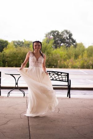 Bride in flowing white dress with lace detail poses on outdoor patio with decorative benches.