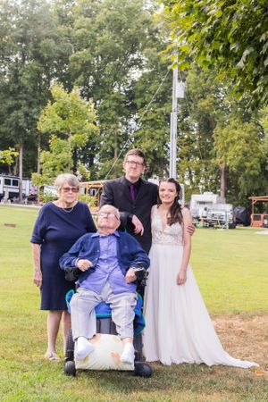 A group photo of wedding party members and family on a grassy lawn with trees in background.