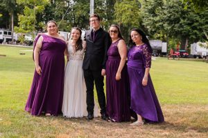 Wedding party wearing purple bridesmaid dresses poses together on grass.