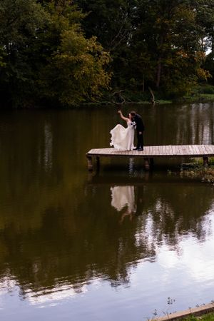 Romantic wedding photo of couple on dock with perfect reflection in calm lake water.