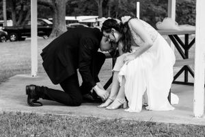 Black and white photo of groom helping bride with her shoes during wedding day.