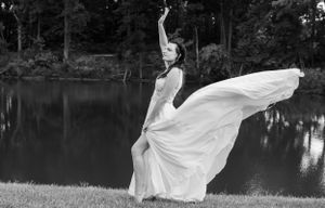 Black and white photo of bride in flowing dress striking dramatic pose by lake.
