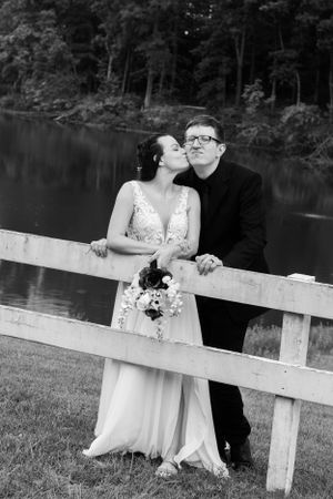 A black and white wedding photo captured on a wooden fence by a peaceful lake.