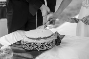 A black and white photo of hands cutting into a decorated wedding cake.