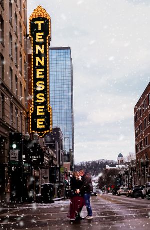 Illuminated Tennessee Theatre sign with falling snow on a city street at dusk.