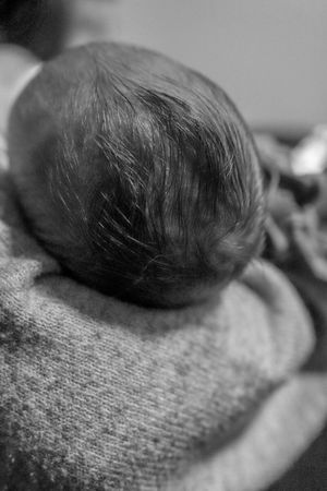 Black and white close-up of a newborn baby's head resting on a knit surface.