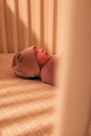 Peaceful sleeping newborn wearing a soft pink hat rests on patterned bedding.