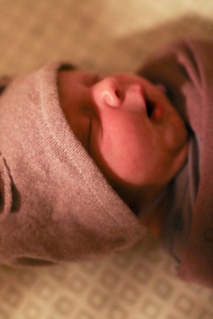 Close-up portrait of a peaceful newborn wrapped in soft gray fabric.