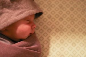 Side profile of a sleeping infant in a pink hat against a patterned background.