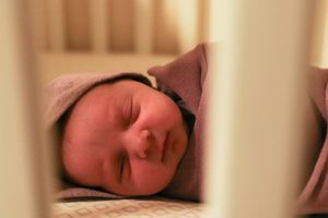 Close-up view through crib slats of a sleeping baby wearing a pink hat.