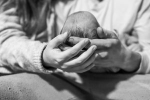 Black and white image of gentle hands cradling a newborn baby.
