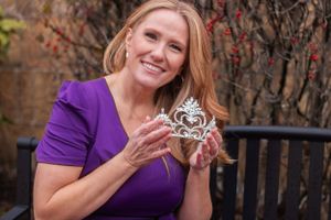 Person in purple blouse holding and admiring a decorative silver tiara.