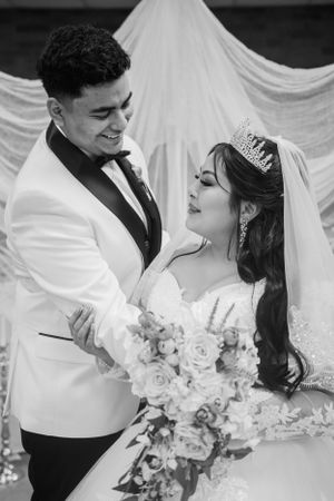 A couple shares a joyful moment in black and white under wedding arch with roses.