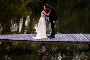 Wedding couple shares a tender moment on a wooden dock over calm waters at dusk.