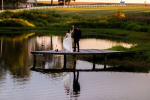 Silhouettes of newlyweds standing on wooden dock with mirror-like water reflections.