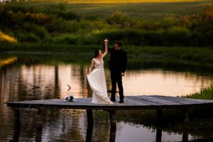 Wedding couple celebrates joyfully on wooden dock during golden hour.