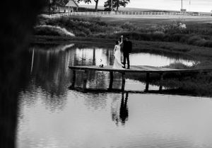 A couple stands on a wooden dock overlooking a peaceful pond with reflections at dusk.