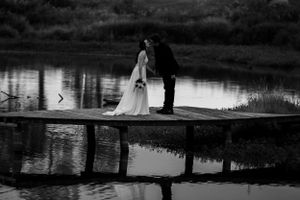 A romantic black and white wedding photo on a wooden dock with reflections in still water.