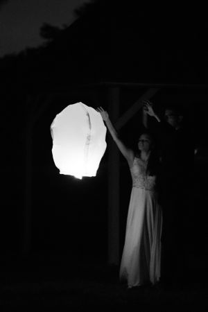 A figure in a white dress releasing a glowing paper lantern into the night sky.