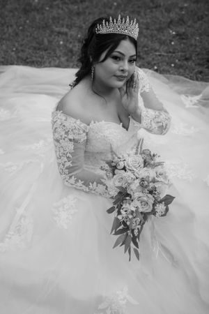 Black and white portrait of bride in lace gown with tiara holding floral bouquet.