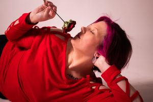 Person in red sweater enjoying a sweet treat against pink backdrop.