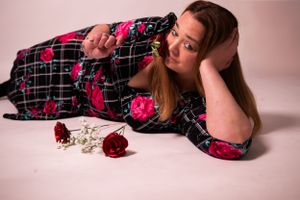 Person in floral print dress lying on white floor with red roses.