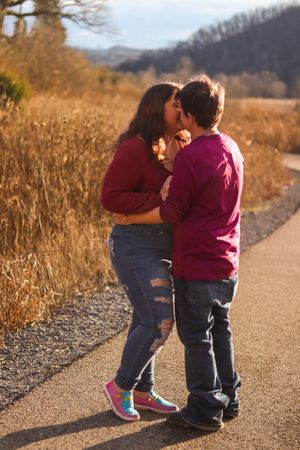 A couple in matching burgundy sweaters embrace on a nature trail during golden hour.