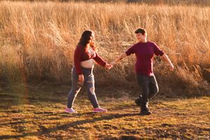 A couple dances playfully on a path with golden grass in the background.