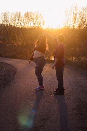 Two silhouettes stand on a path at sunset with tall grass surrounding them.