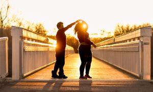 A couple dances on a wooden bridge at sunset creating romantic silhouettes.