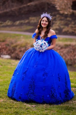 Woman in a stunning royal blue ball gown with crown holding a floral bouquet.