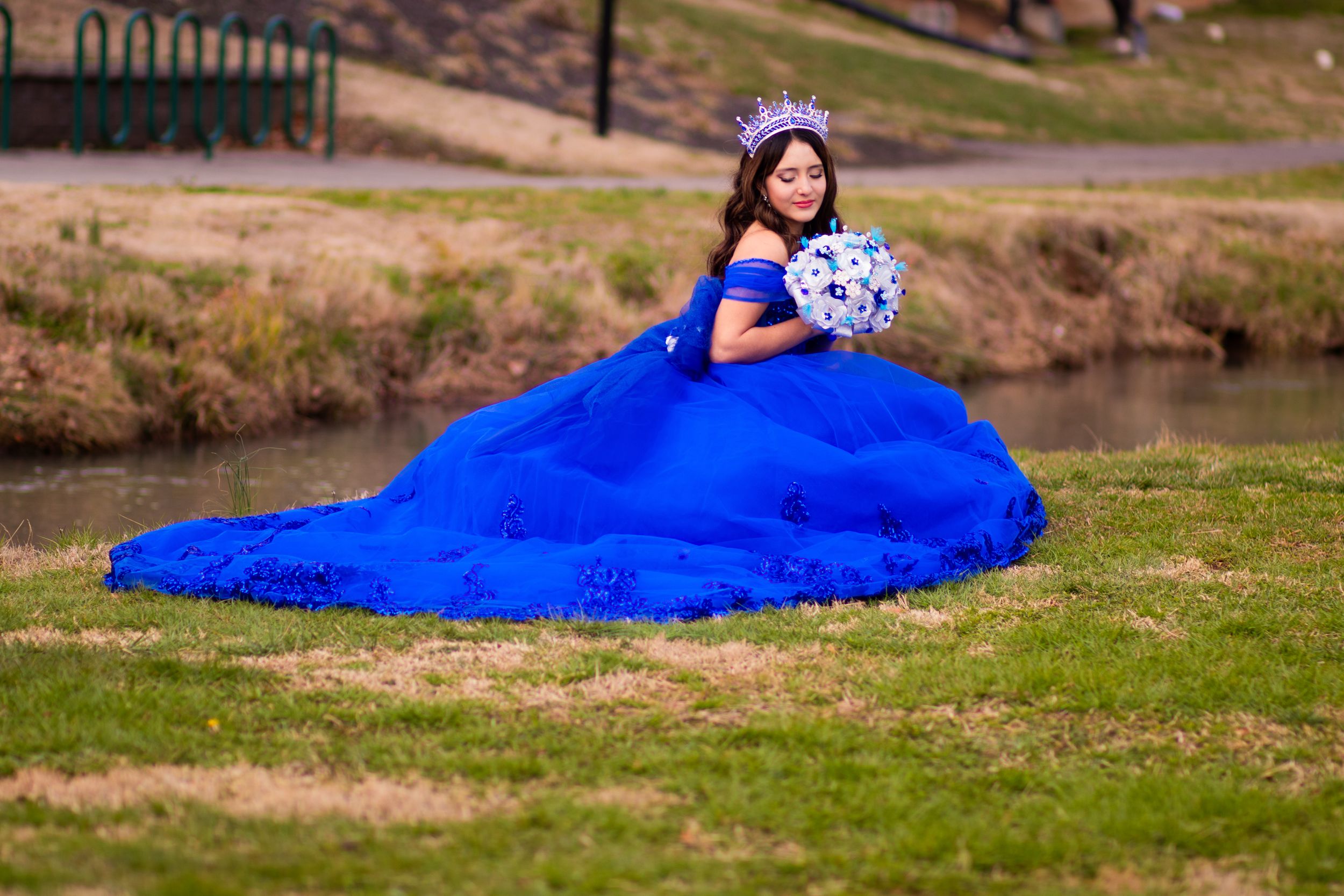 Beautiful royal blue ball gown spreads across green grass near water.