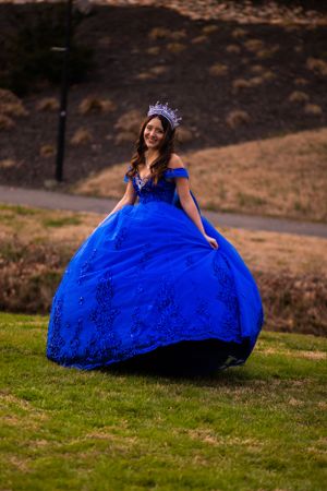 A magnificent blue quinceañera dress with a voluminous skirt on a grassy hillside.