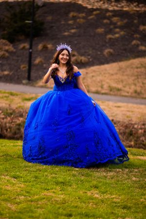 A princess-style royal blue ball gown with off-shoulder design photographed outdoors.