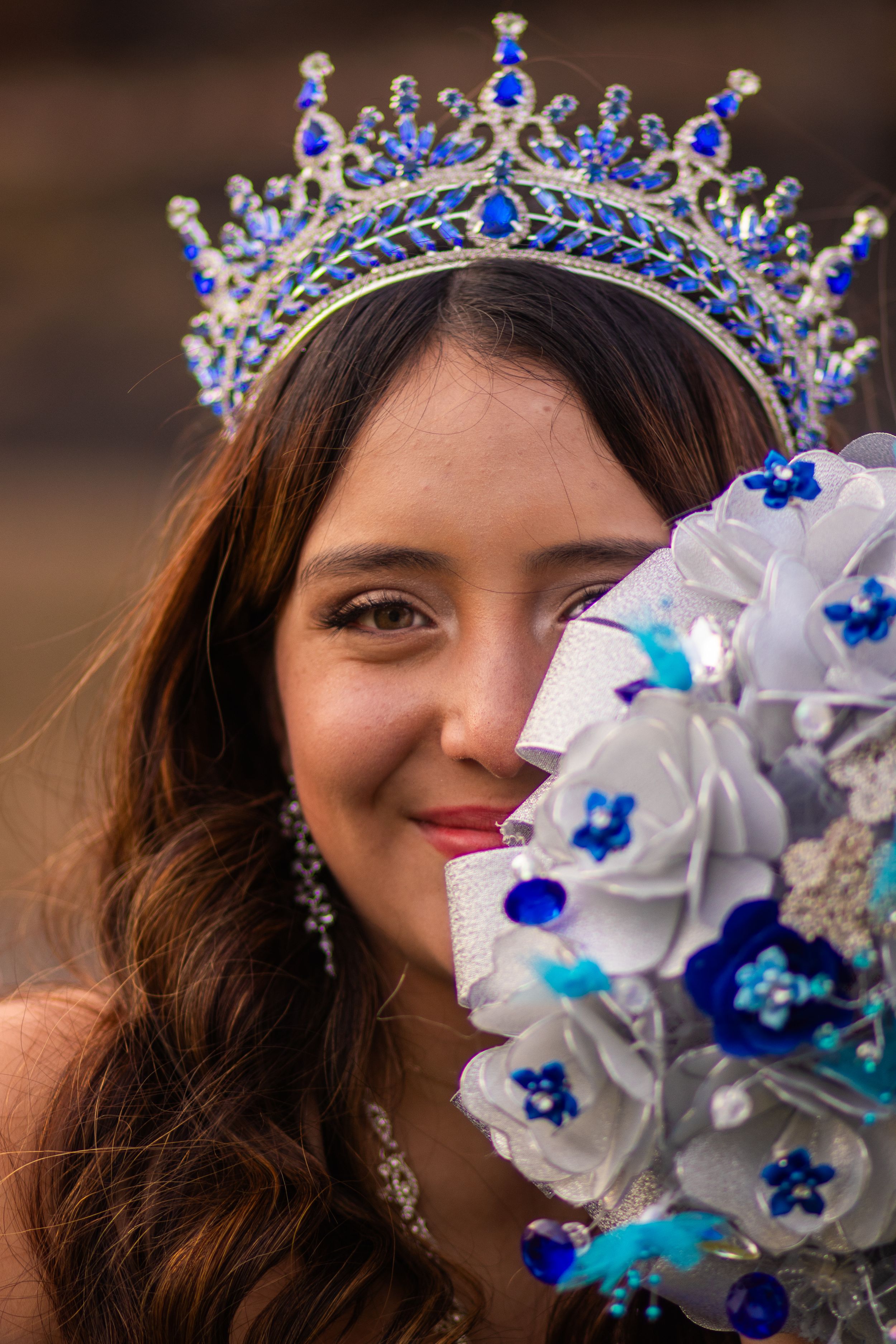 Elegant blue and silver crown adorns flowing dark hair with white floral bouquet.