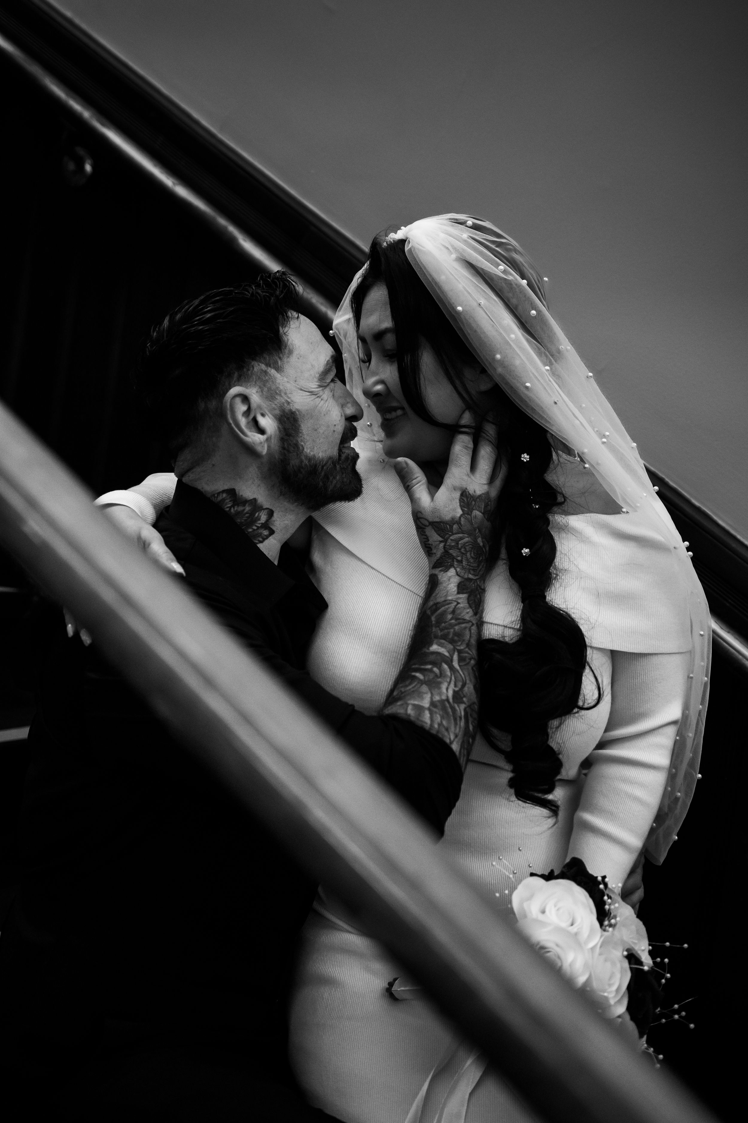 Dramatic black and white portrait of couple sharing tender moment on staircase.