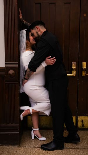 A romantic couple in wedding attire share an intimate moment against a wooden door.