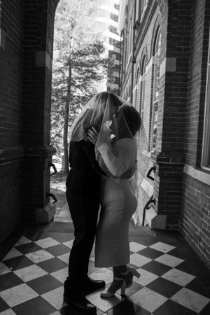 Black and white photo of newlyweds sharing an intimate moment under an archway.