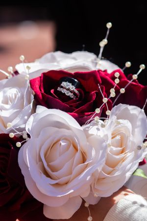 A diamond ring nestled in a deep red rose surrounded by white roses and pearl accents.