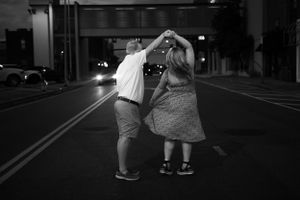 A couple dances together on a dimly lit city street at night.