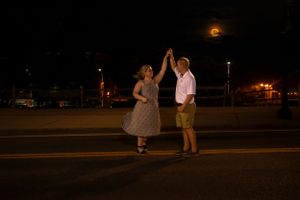 A couple shares a romantic dance moment under moonlight in a parking lot.