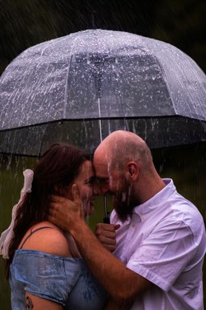 A couple shares an intimate moment under a clear umbrella in the rain.