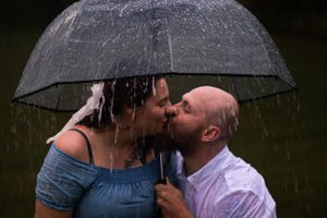 A couple shares a kiss under a clear umbrella as rain falls around them.