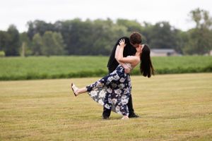 A romantic dip pose between a couple in a floral dress and dark attire on a grassy field.