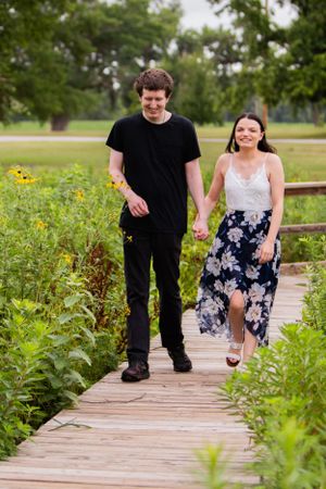 A couple walking and laughing together on a wooden boardwalk surrounded by wildflowers.