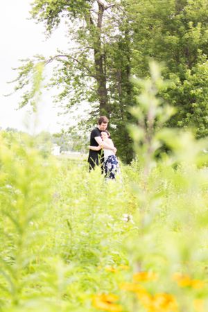Romantic outdoor portrait in a lush meadow with wildflowers and trees in soft summer light.