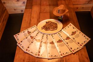 A steak dinner and cowboy hat arranged with playing cards on rustic wooden table.