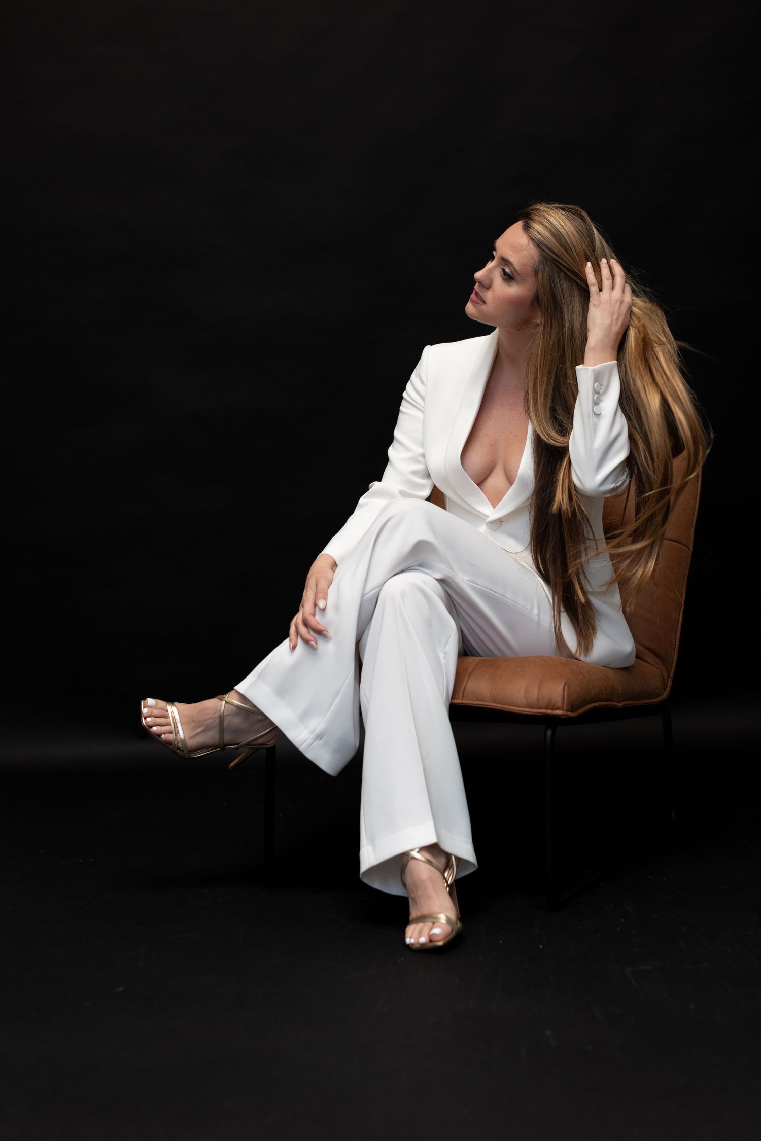 A striking fashion portrait featuring a white pantsuit and strappy heels against a dark background.